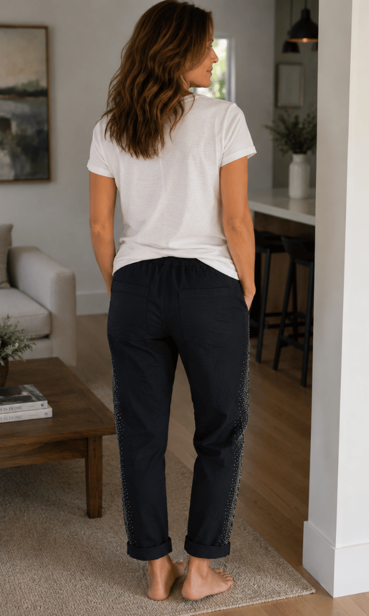 Woman standing in a living room wearing a white t-shirt and black pants.