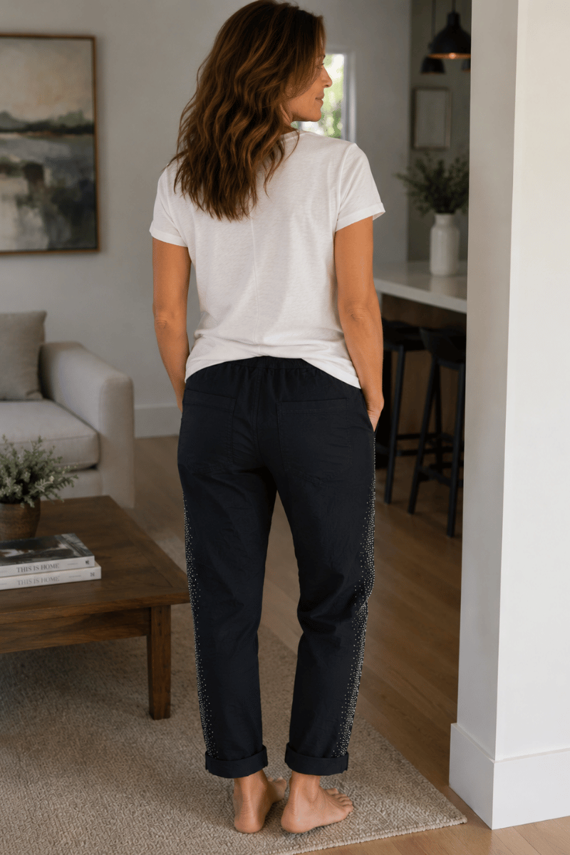 Woman standing in a living room wearing a white t-shirt and black pants.