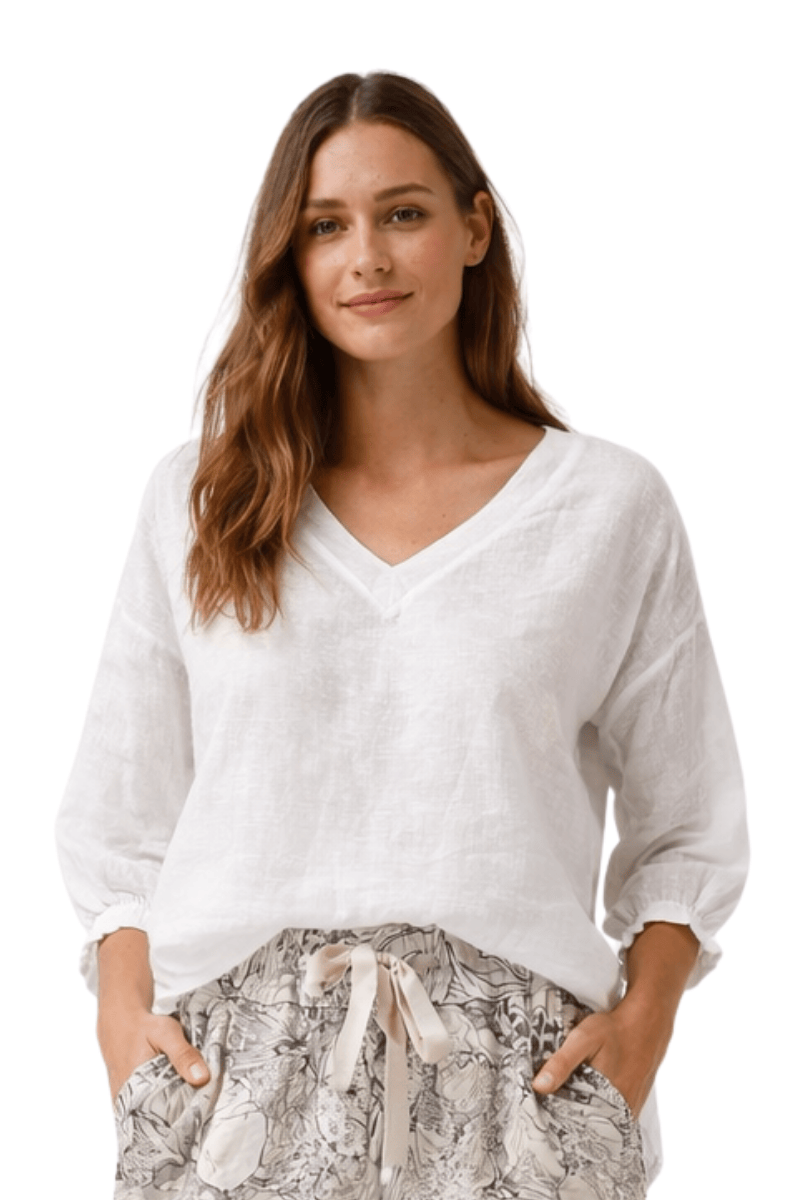Woman wearing a white V-neck sweater and patterned pants on a white background