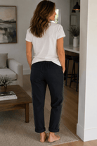 Woman standing in a living room wearing a white t-shirt and black pants.